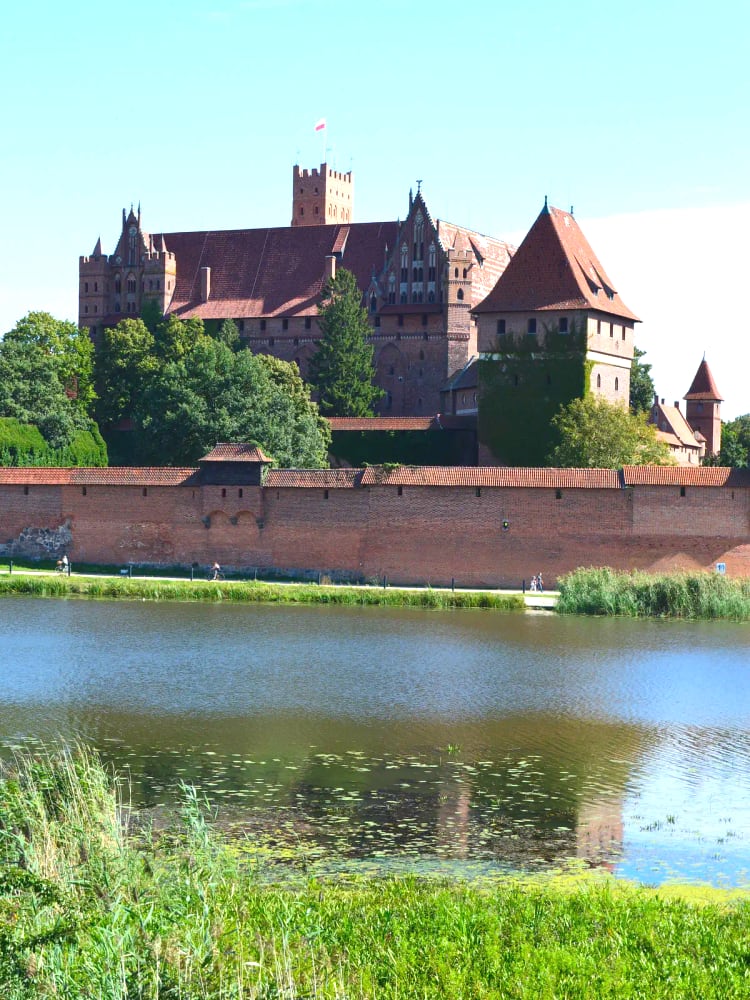 Malbork Castle (Zamek w Malborku) reflected in the Nogat river — the largest brick castle in the world, built by the Teutonic Order from 1274, reconstructed after WWII damage, UNESCO 1997.